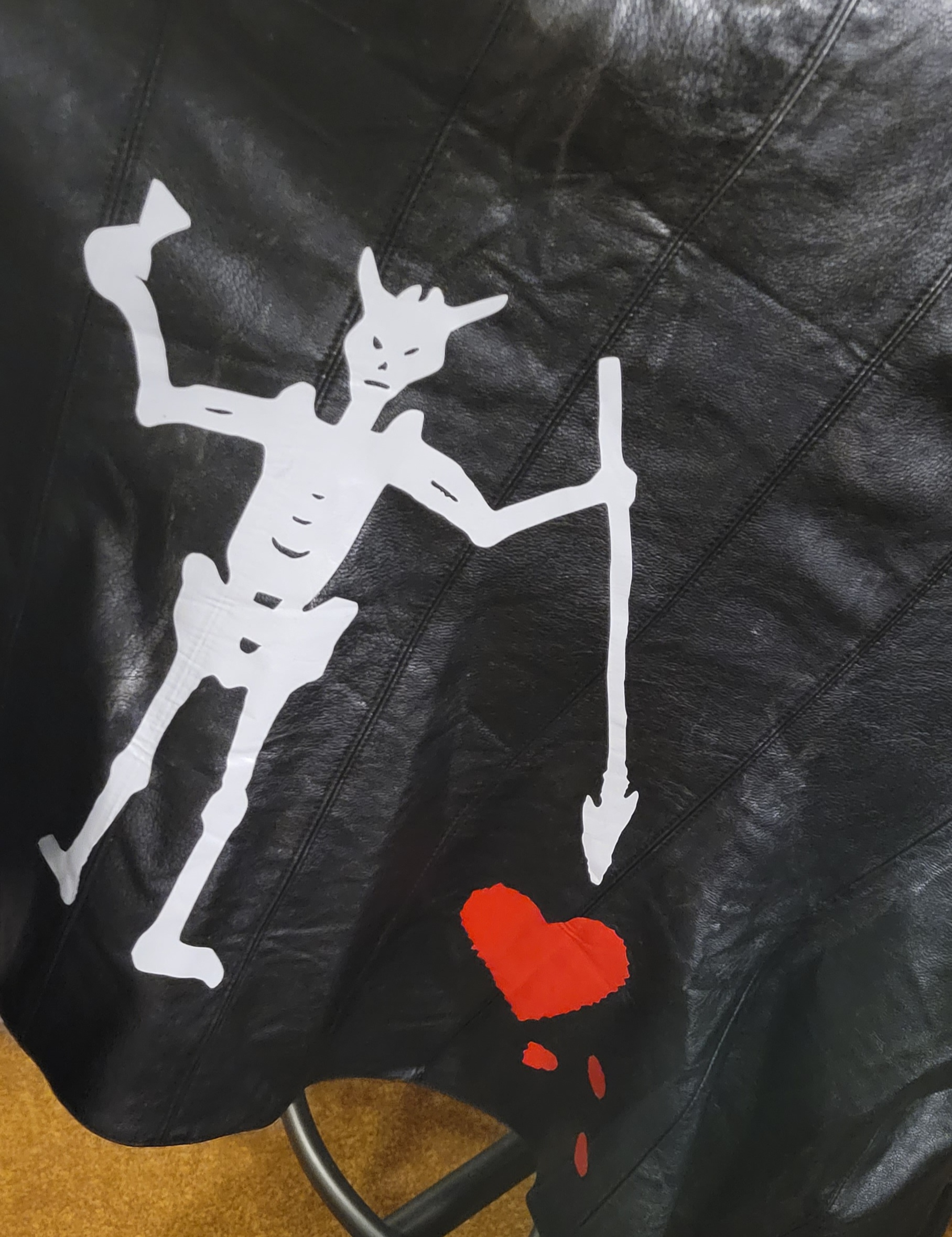 The back of my black pleather vest with the white vinyl cutout of Blackbeard's flag's demon skeleton harpooning a red vinyl cutout of a bleeding heart.